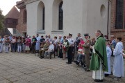 Uczestnicy uroczystości i kombatanci stoją przed kościołem.