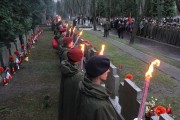 Harcerze z pochodniami stoją przed mogiłami powstańców na Powązkach. 