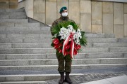 Żołnierz stoi z wiązanką biało-czerwonych kwiatów