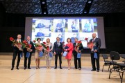 Wyróżnieni pracownicy spółki stoją na scenie z kwiatami i nagrodami. 