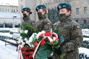 Asysta wojskowa stoi z wiązanką biało-czerwonych kwiatów 