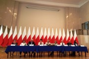 Prelegenci konferencji siedzą za stołem. W tle biało-czerwone flagi. 