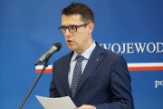 Wystąpienie przedstawiciela IPN na tle niebieskiej ścianki z napisem wojewoda wielkopolski