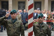 Dwaj żołnierze salutują przed flagą na maszcie na tle uczestników uroczystości