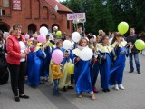 Dzieci z kolorowymi balonikami stoją przed kościołem.