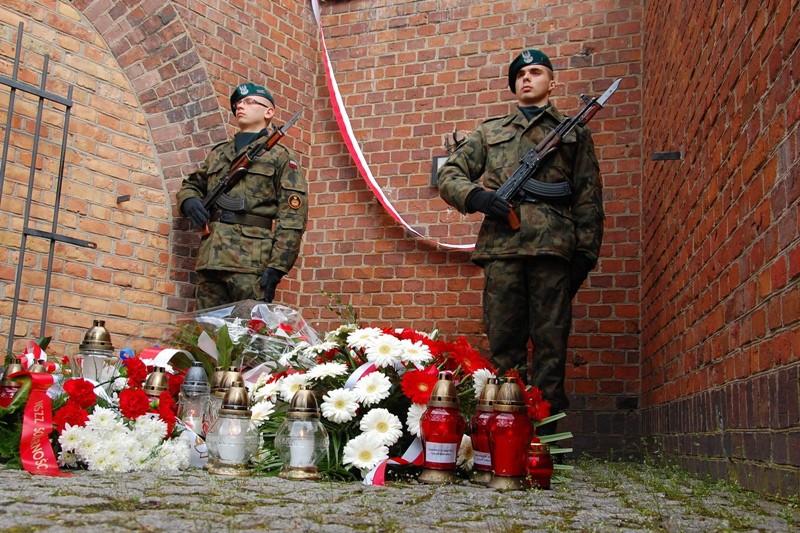 Zbliżenie na wieńce i wartę honorową pod ścianą śmierci.