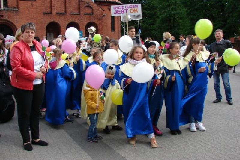 Dzieci z kolorowymi balonikami stoją przed kościołem.