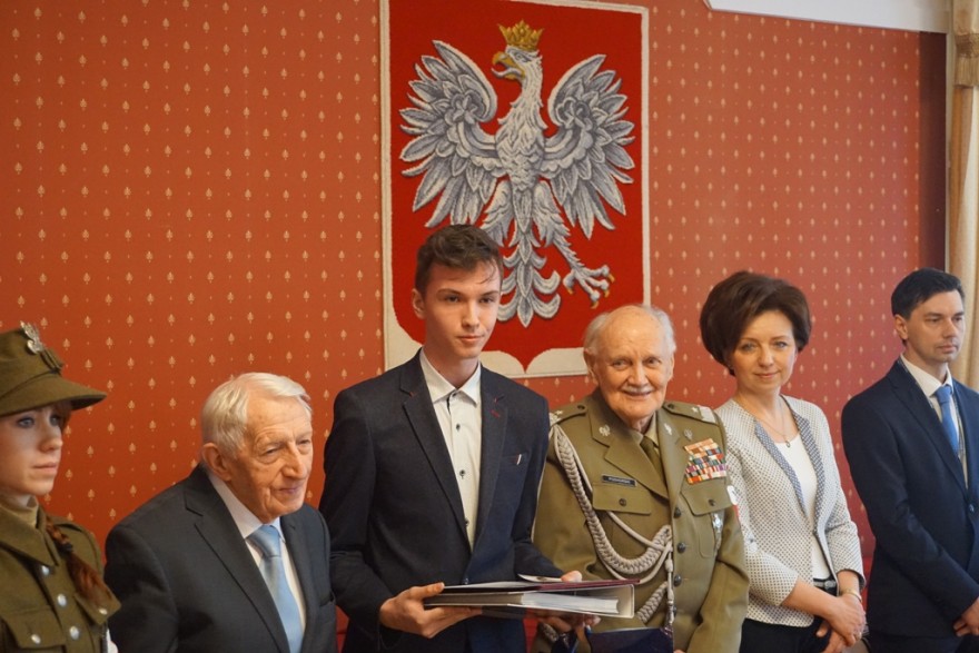 Wicewojewoda, generał Jan Podhorski i kombatanci wraz z laureatami konkursu - zdjęcie na tle godła.