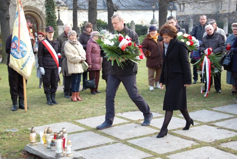 Wicewojewoda wielkopolski podchodzi w towarzystwie niosącego wieniec do pomnika, żeby złożyć wieniec. 